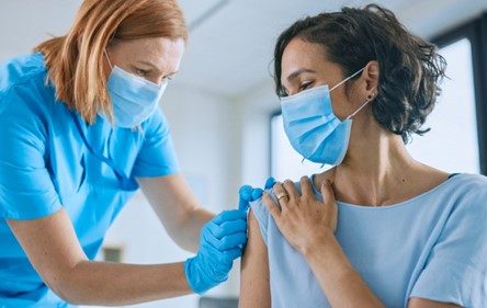 Masked man receives vaccination on arm by a female medical professional